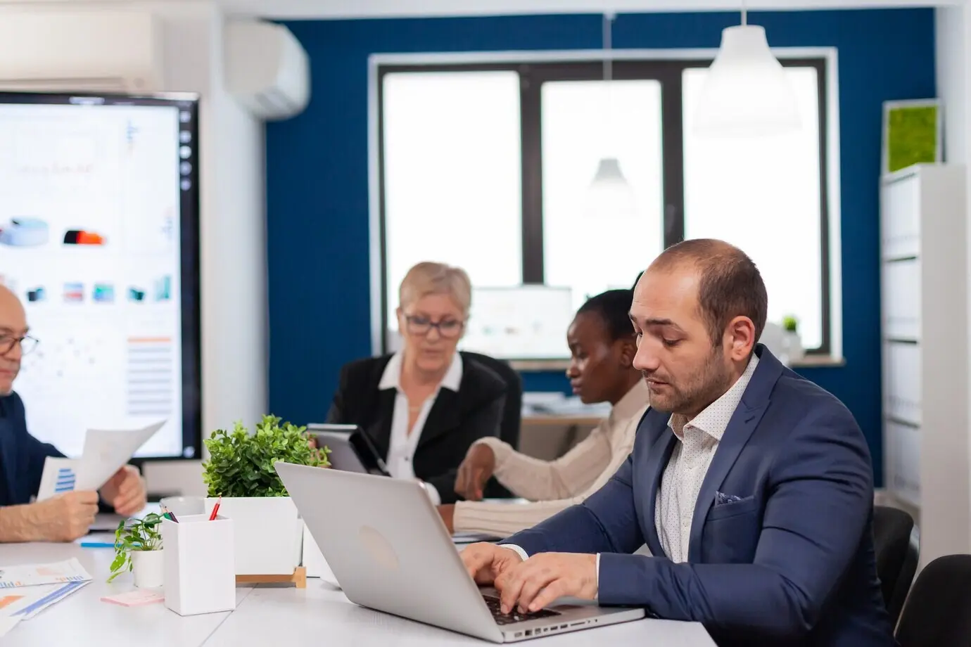 Busy businessman sitting at a conference table in a boardroom, typing on a laptop and focused on his work.